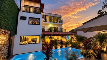 Un edificio moderno de dos pisos con piscina, asientos al aire libre y vista al atardecer.