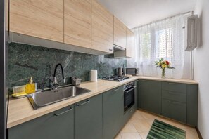 A kitchen with a sink, stove, microwave, and cabinets. - Warsaw Praga Apartment — Balcony & Metro Nearby (Warszawa)