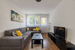 Ein modernes Wohnzimmer mit einem grauen Ecksofa, einem schwarzen Couchtisch, einem Flachbildfernseher und einem Gemälde an der Wand.