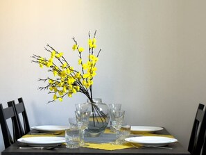 Ein Esstisch mit Geschirr, Besteck und einer Vase mit gelben Blumen.