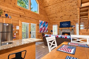 A cabin interior with a kitchen, dining area, and fireplace. - Douglas Lake Cabin | Hot Tub, Loft & Sleeps 7 (Sevierville)
