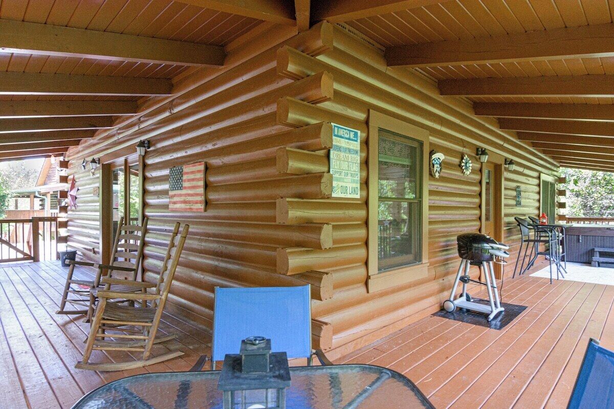 A log cabin with a wooden deck, a glass table, and a rocking chair.