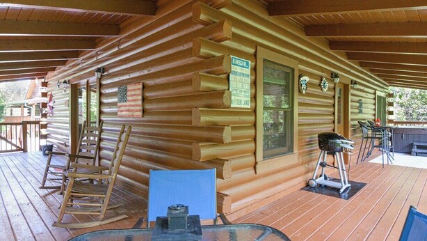 A log cabin with a wooden deck, a glass table, and a rocking chair. - Douglas Lake Cabin | Hot Tub | Sleeps 7 (Sevierville)