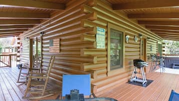 A log cabin with a wooden deck, a glass table, and a rocking chair.