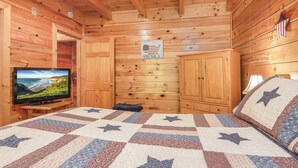 A room with wooden walls, a television on a stand, a bed with a star-patterned quilt, and a sign that says 'AMERICA'. - Douglas Lake Cabin | Hot Tub | Sleeps 7 (Sevierville)
