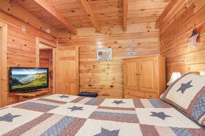A room with wooden walls, a television on a stand, a bed with a star-patterned quilt, and a sign that says 'AMERICA'. - Douglas Lake Cabin | Hot Tub | Sleeps 7 (Sevierville)