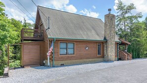 A log cabin with a stone chimney, a porch, and an American flag. - Douglas Lake Cabin | Hot Tub | Sleeps 7 (Sevierville)