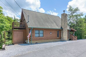A log cabin with a stone chimney, a porch, and an American flag. - Douglas Lake Cabin | Hot Tub | Sleeps 7 (Sevierville)
