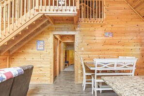 A wooden cabin interior with a staircase leading to a balcony, a dining area with a table and chairs, and a small hallway. - Douglas Lake Cabin | Hot Tub, Loft & Sleeps 7 (Sevierville)