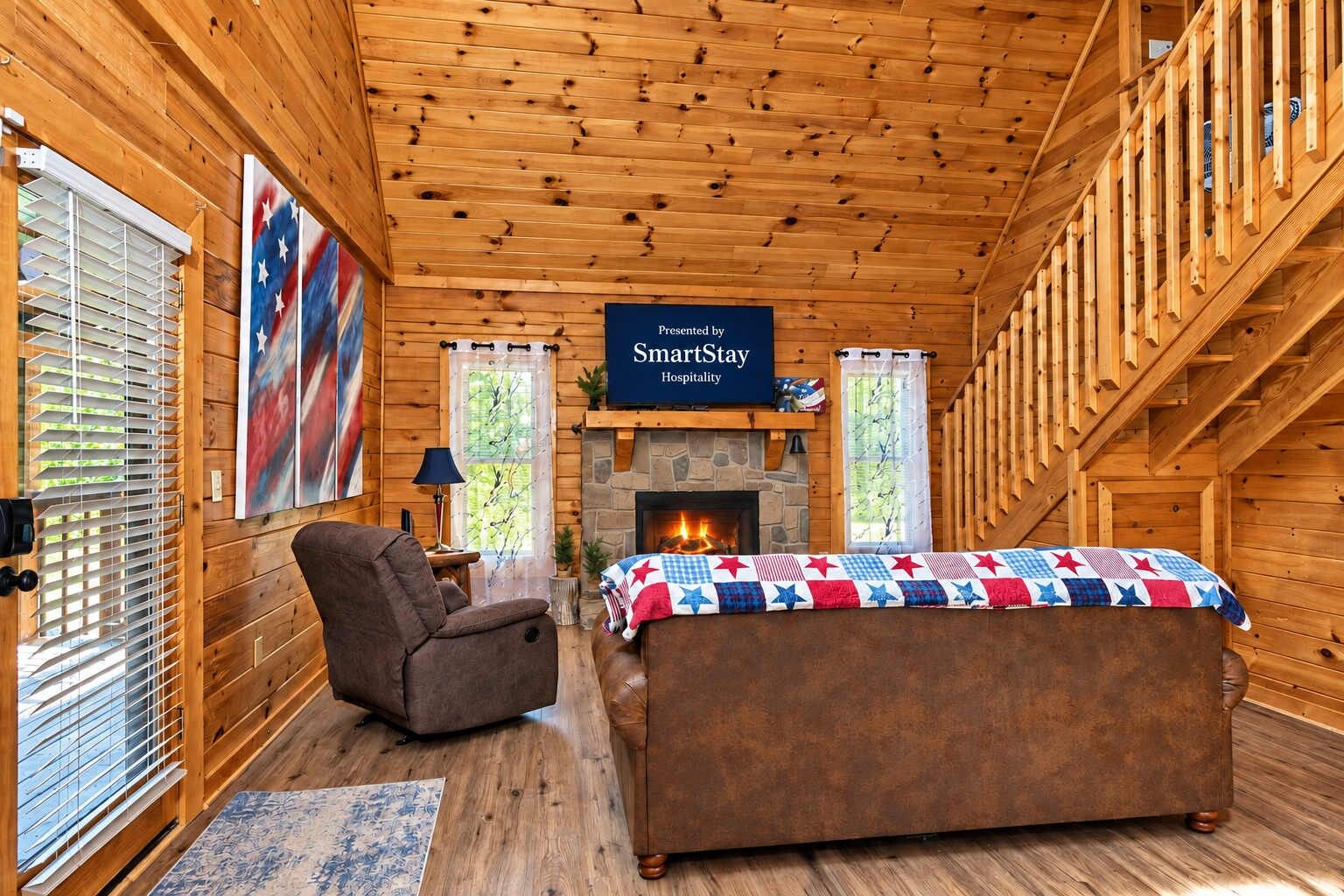 Una camera in una baita con camino, un letto con copriletto a tema patriottico, una sedia e un cartello per SmartStay Hospitality.