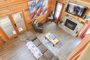 A cozy cabin interior with a fireplace, a sofa, a coffee table, and a television. - Douglas Lake Cabin | Hot Tub | Sleeps 7 (Sevierville)