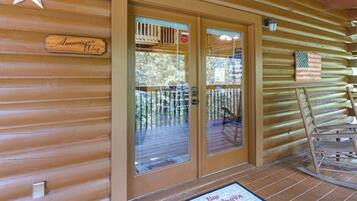 Une cabane en bois avec une enseigne indiquant « American Way », une entrée avec une porte en verre, une terrasse avec des chaises et un drapeau américain.