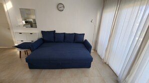 Ein Schlafzimmer mit einem großen Bett, einem Nachttisch, einem Spiegel, einer Uhr und einem Fenster mit Vorhängen.