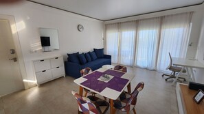 A modern living room with a sofa, a dining table, and a TV mounted on the wall. - Modern 1BR Sosúa Ocean Village 100 Mbps Wi-Fi (Sosúa)