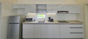 Eine kleine Küche mit weißen Schränken, einer Mikrowelle, einem Mixer, einer Kaffeemaschine und einem Kühlschrank.