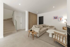 A modern living room with a staircase, a sectional sofa, a round coffee table, and a TV. - Casa Floresta - Private Pool Retreat (Óbidos)