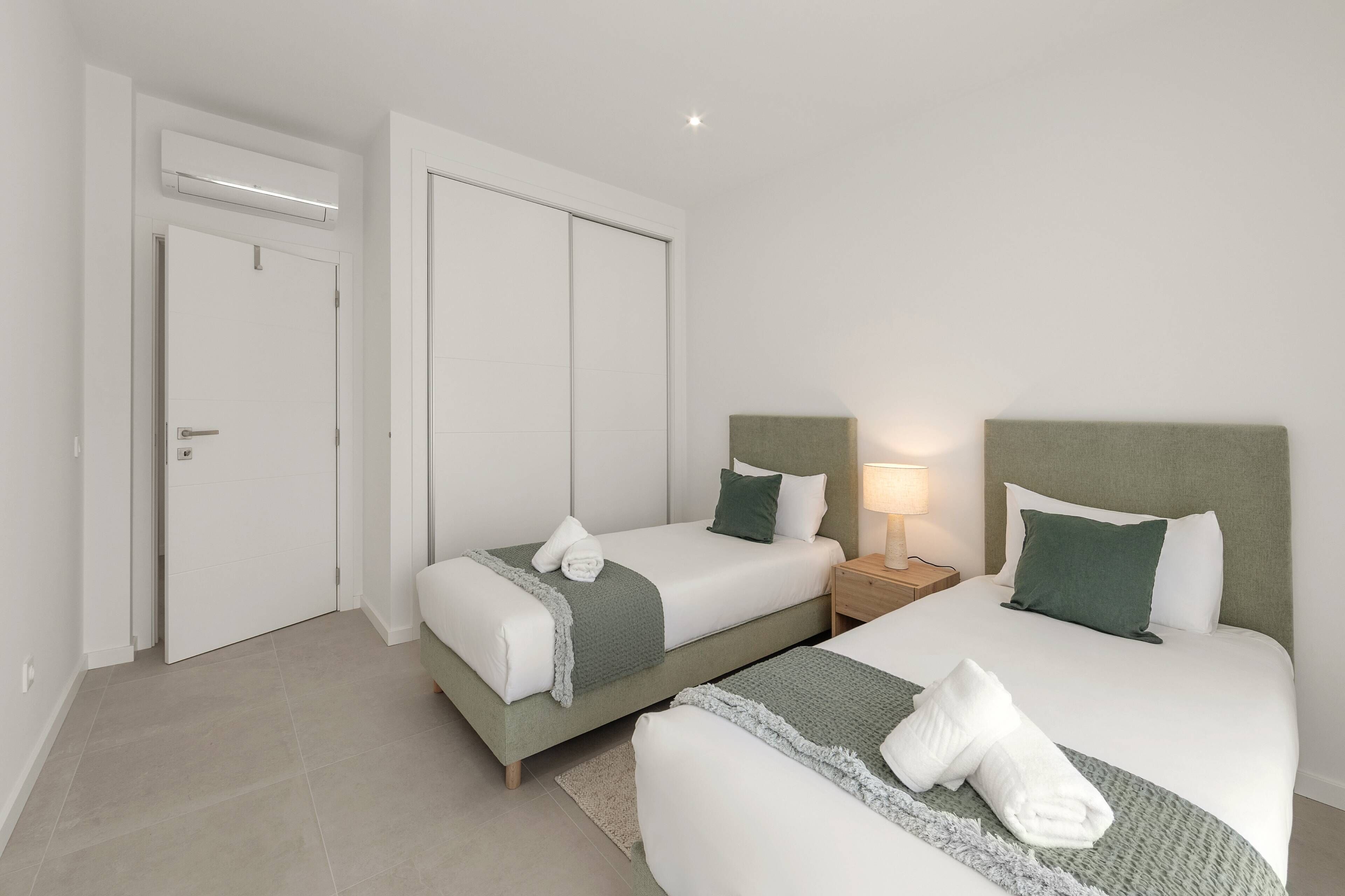 Una habitación de hotel con dos camas, un armario, una mesita de noche con lámpara y una puerta.