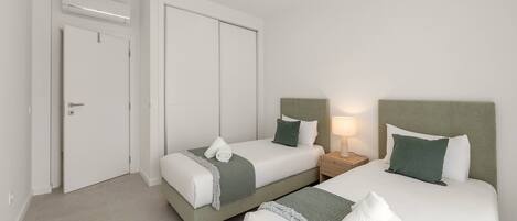 Una habitación de hotel con dos camas, un armario, una mesita de noche con lámpara y una puerta.