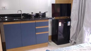 Une petite cuisine équipée d’une cuisinière, d’un évier et d’un réfrigérateur, un lit avec une couvre-lit à motifs et un mur en briques.