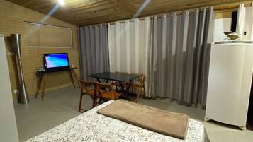 A room with a bed, a desk with a computer, a dining table with chairs, and a refrigerator.