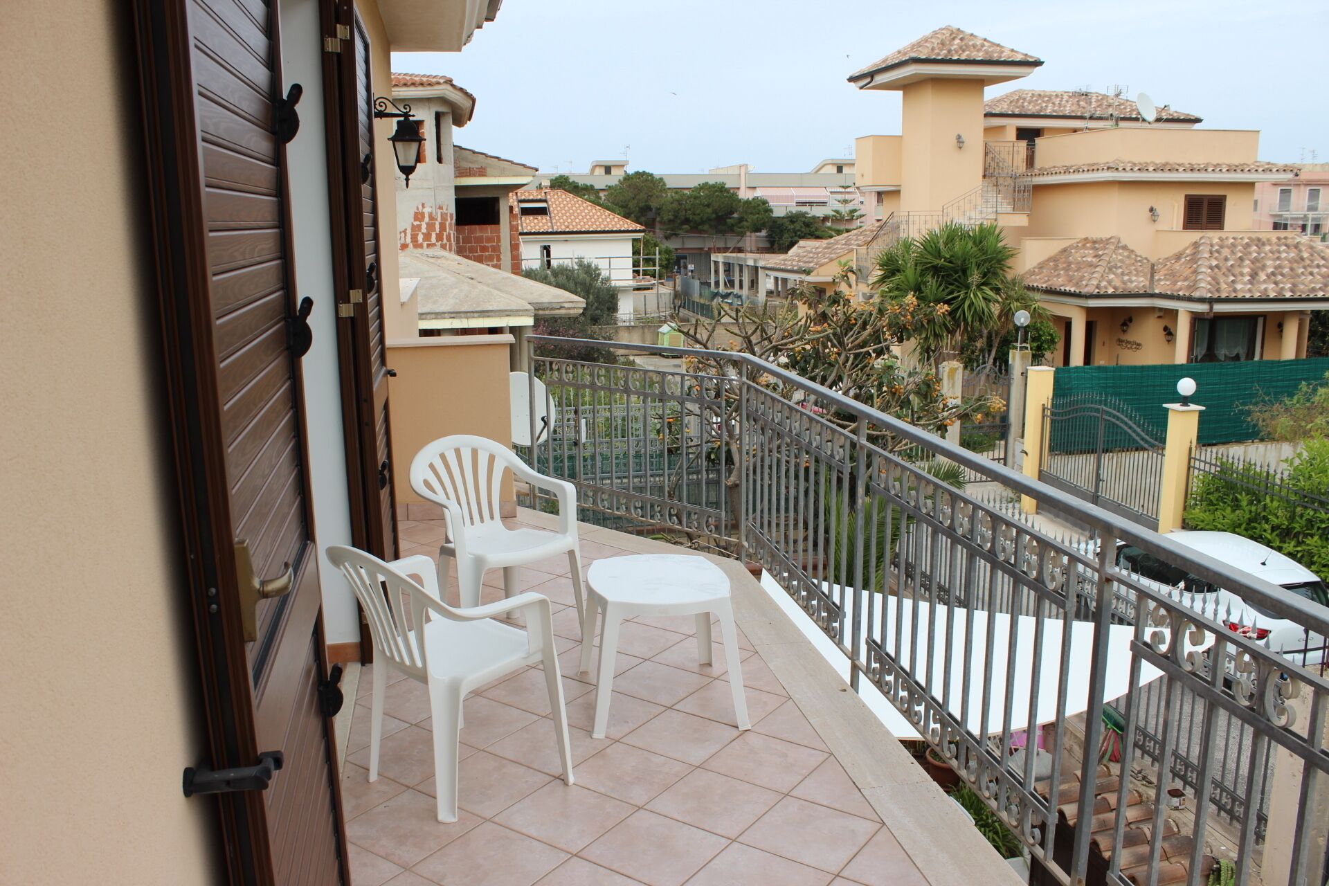 A balcony with two white plastic chairs and a small table, surrounded by a metal railing.