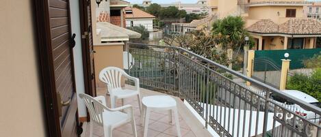 A balcony with two white plastic chairs and a small table, surrounded by a metal railing.