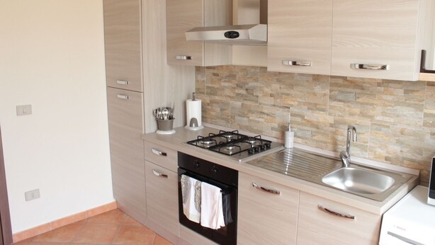 Een moderne keuken met lichte houtkleurige kastjes, een gasfornuis, een roestvrijstalen spoelbak en een betegelde achterwand.