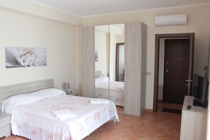 A hotel room with a bed, a nightstand, a TV, and a door. - Villa Alsorriso (Isola delle Femmine)