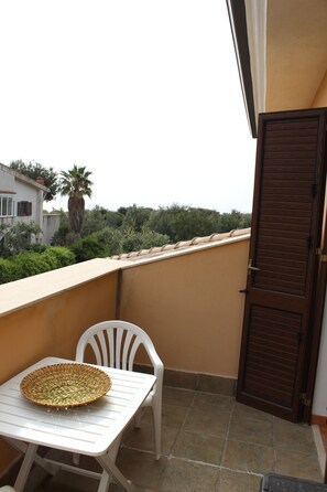 A balcony with a table, a wicker basket, and a white plastic chair. - Villa Alsorriso (Isola delle Femmine)