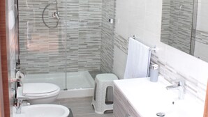 Een moderne badkamer met een glazen douchecabine, toilet, bidet en een wastafelmeubel met spiegel.