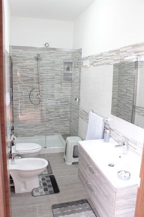 A modern bathroom with a glass shower enclosure, a white toilet, a bidet, and a vanity with a mirror. - Villa Alsorriso (Isola delle Femmine)