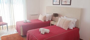 A hotel room with two beds, a nightstand, a lamp, and a chair. - Blue Horizon, Praia del Rey apartment B9 (Óbidos)