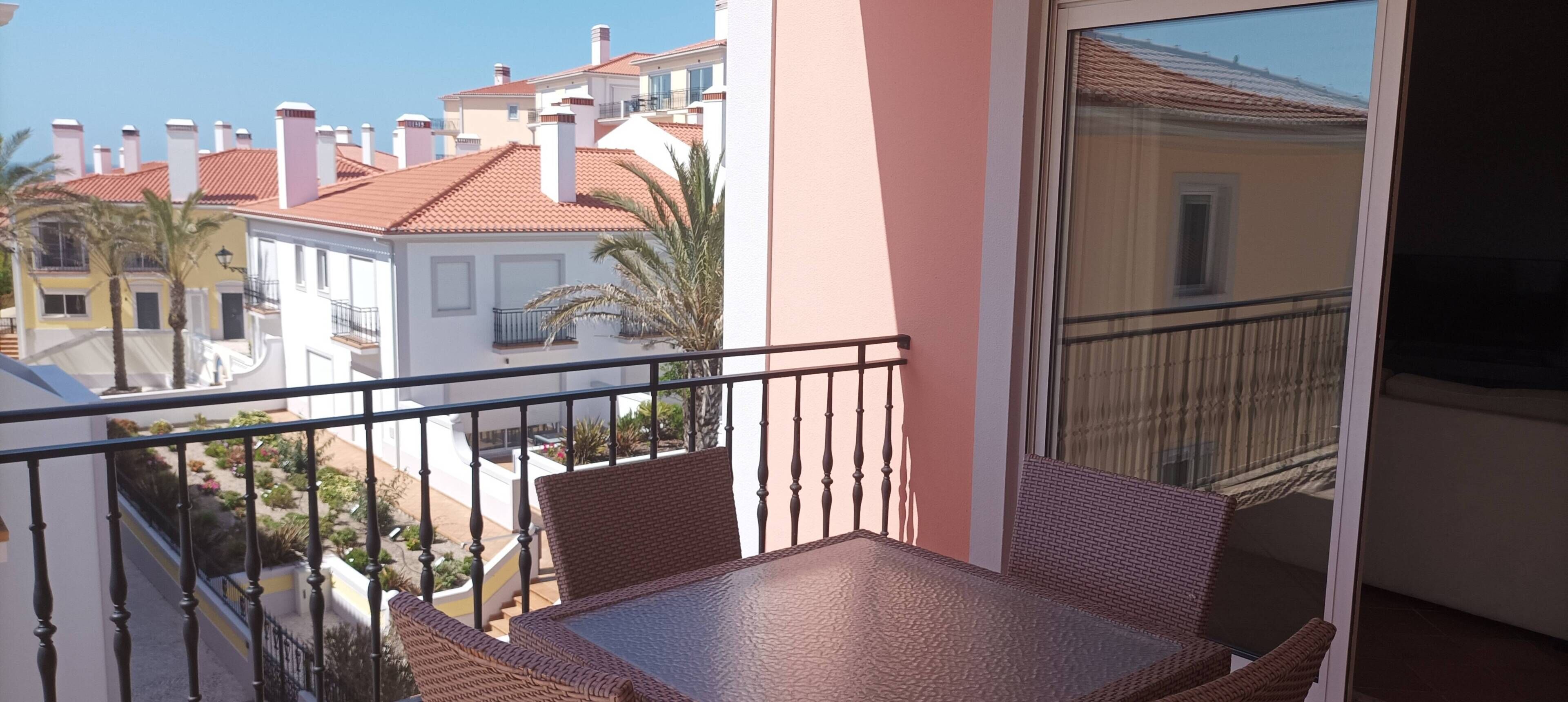 A balcony with wicker furniture, a glass door, and a view of neighboring buildings.