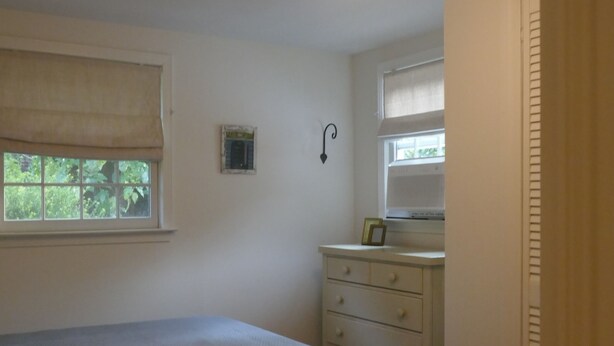 A bedroom with a bed, a dresser, a nightstand, a window with blinds, and a ceiling light fixture.