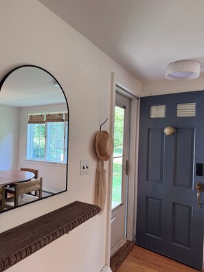 Una habitación con suelo de madera, una puerta azul oscuro, un espejo y una ventana con persianas.