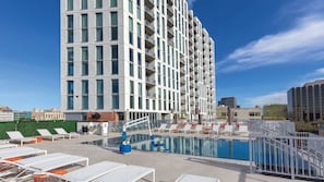 Um hotel moderno com piscina no terraço, espreguiçadeiras e vista clara da paisagem urbana circundante.