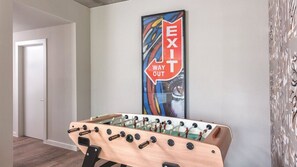 Quarto com mesa de futebol, uma porta e parede com a placa 'EXIT WAY OUT'.