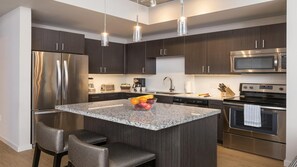 Cozinha moderna com armários de madeira escura, eletrodomésticos de aço inoxidável, bancadas de granito e uma ilha central com assentos.