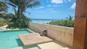 A swimming pool with a wooden deck, surrounded by palm trees and a view of the ocean. - Beachfront House: Pool, kayaks, and a large terrace. Perfect for families. Pet-Friendly. (Telchac)