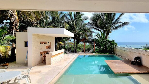 Ein moderner Poolbereich mit freiem Blick auf den Ozean, umgeben von Palmen und einem weißen Gebäude mit Balkon.