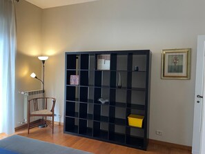 Ein Zimmer mit einem schwarzen Bücherregal, einem Sessel, einer Stehlampe und einem gerahmten Bild an der Wand.