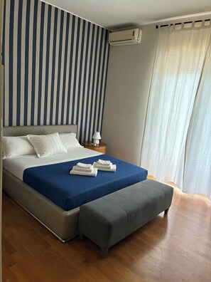 Ein Schlafzimmer mit Bett, Nachttisch, Lampe, Klimaanlage und Vorhängen.
