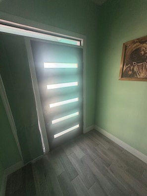 A hallway with a door illuminated by horizontal light strips, a wooden floor, and a framed picture on the wall. - Terrific 4-bedroom townhome with AC in sunny Nassau (Nassau)