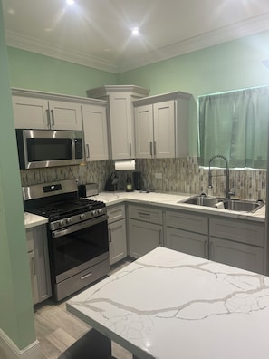 A modern kitchen with stainless steel appliances, white cabinetry, and a marble countertop. - Terrific 4-bedroom townhome with AC in sunny Nassau (Nassau)