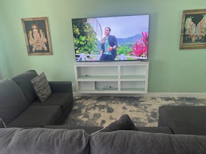 A living room with a flat-screen TV on a white stand, a dark-colored sofa, and a patterned rug. - Terrific 4-bedroom townhome with AC in sunny Nassau (Nassau)