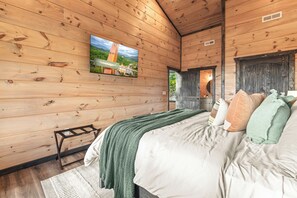 A wooden-paneled bedroom with a bed, pillows, a TV, and a small table. - Hot Tub + Fire Pit | 3BR Cabin Near Dollywood (Sevierville)