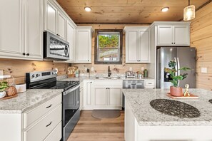 A kitchen with white cabinets, stainless steel appliances, granite countertops, and a wooden ceiling. - Hot Tub + Fire Pit | 3BR Cabin Near Dollywood (Sevierville)