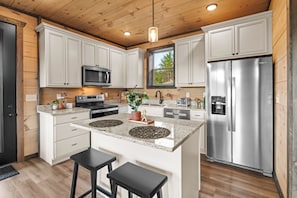 A modern kitchen with white cabinetry, a stainless steel refrigerator, a microwave, and a granite countertop. - Sleeps 10, Hot Tub, Fire Pit, Arcade Game Room, 15 Min to Dollywood (Sevierville)