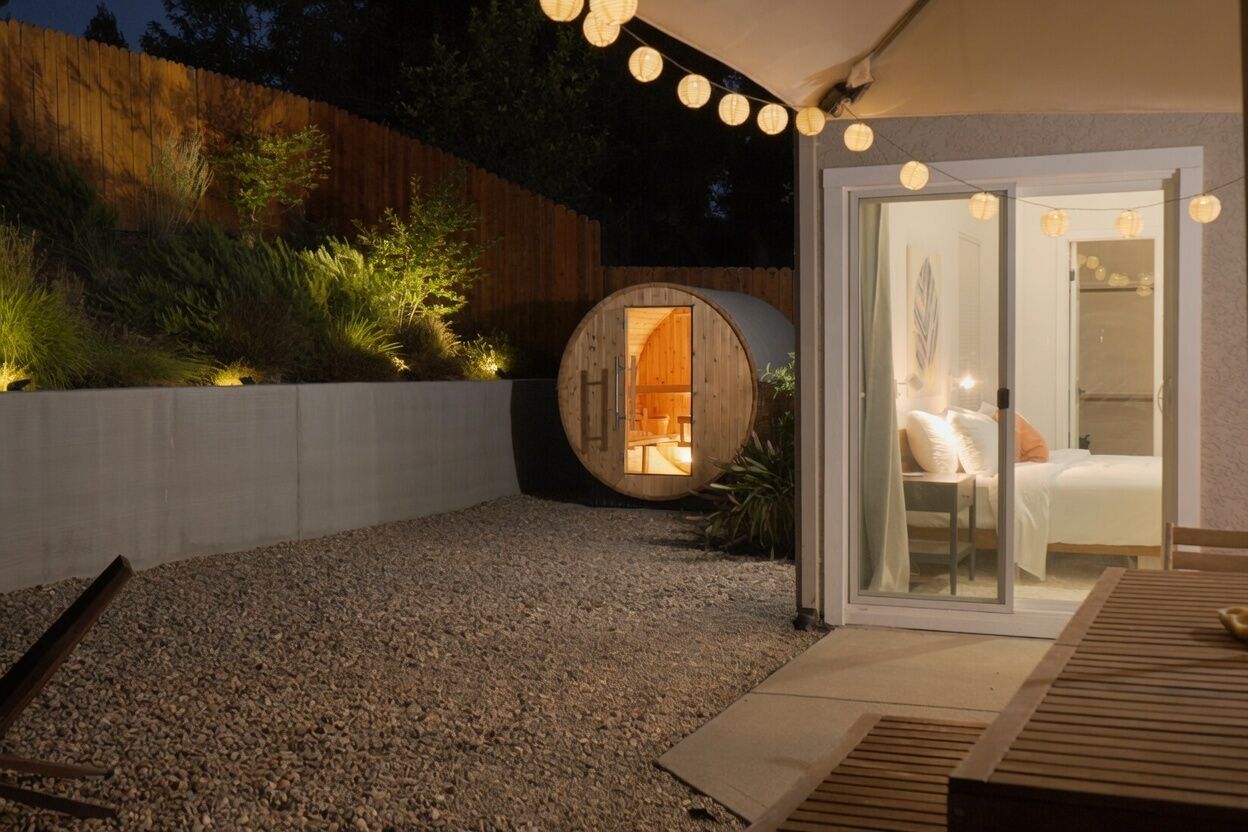 A circular wooden structure with a glass door, a seating area with a table, and a gravel ground.