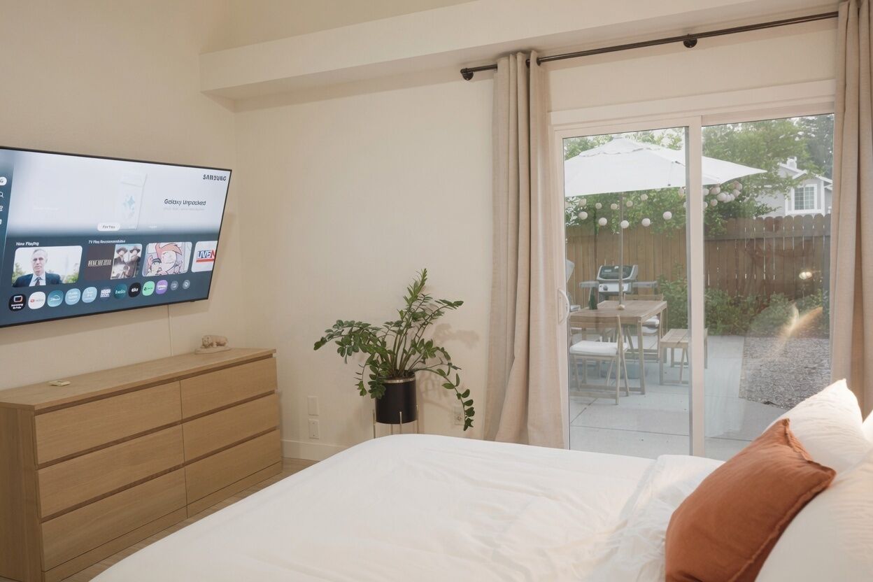 Ein Schlafzimmer mit einem Bett, einem an der Wand montierten Fernseher, einem Blumentopf und einer Schiebetür zu einer Terrasse.